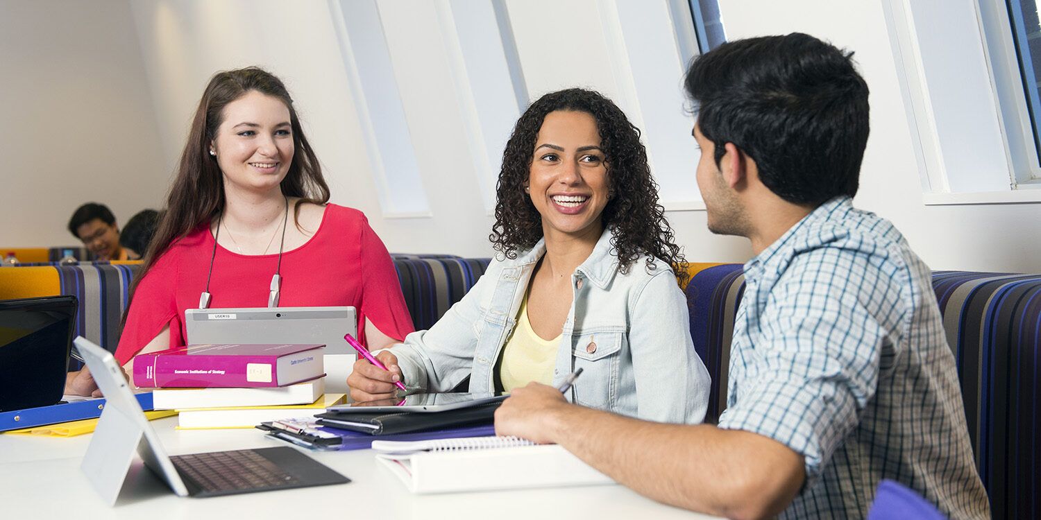 Three people sitting and chatting on a desk indoors