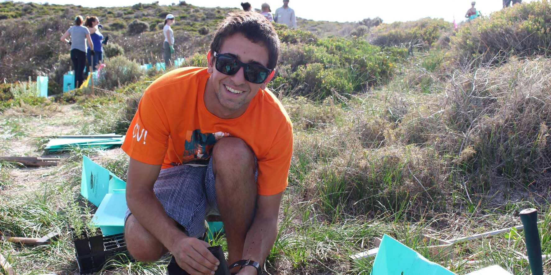 Man in orange shirt planting trees in a field outdoors