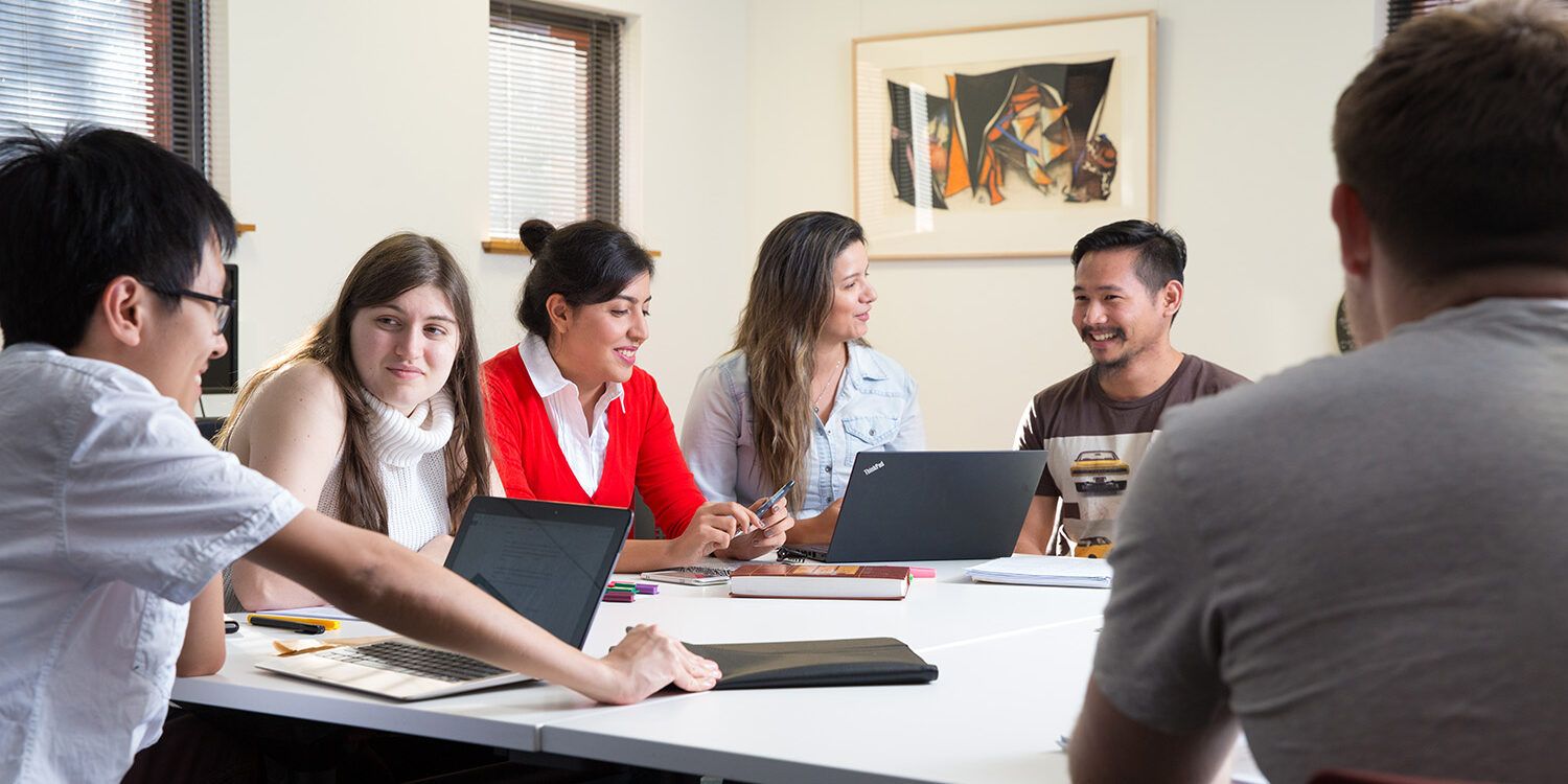 Six people sitting around a desk talking in a room - play video