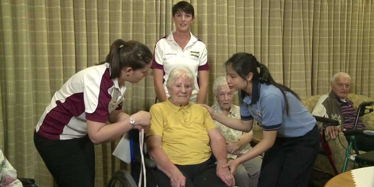 Three students assist an old woman to stand-up - play video