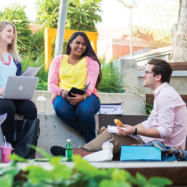 Three people talking to each other outside, with one person eating a donut