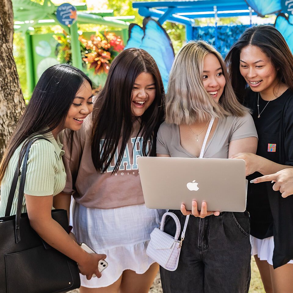 Group of four students talking while looking at a laptop