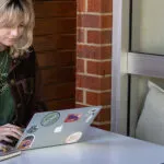 A female student sitting in a cafe, wearing headphones and typing on a laptop