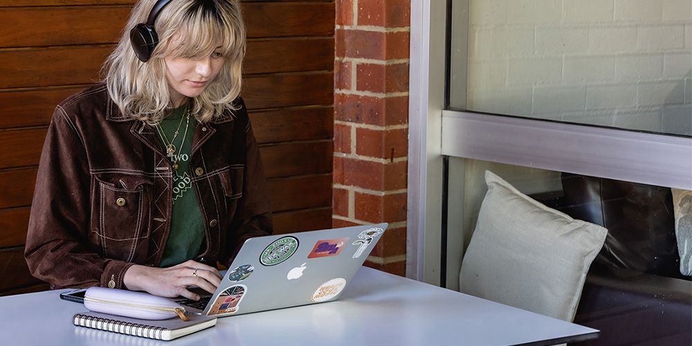 A female student sitting in a cafe, wearing headphones and typing on a laptop