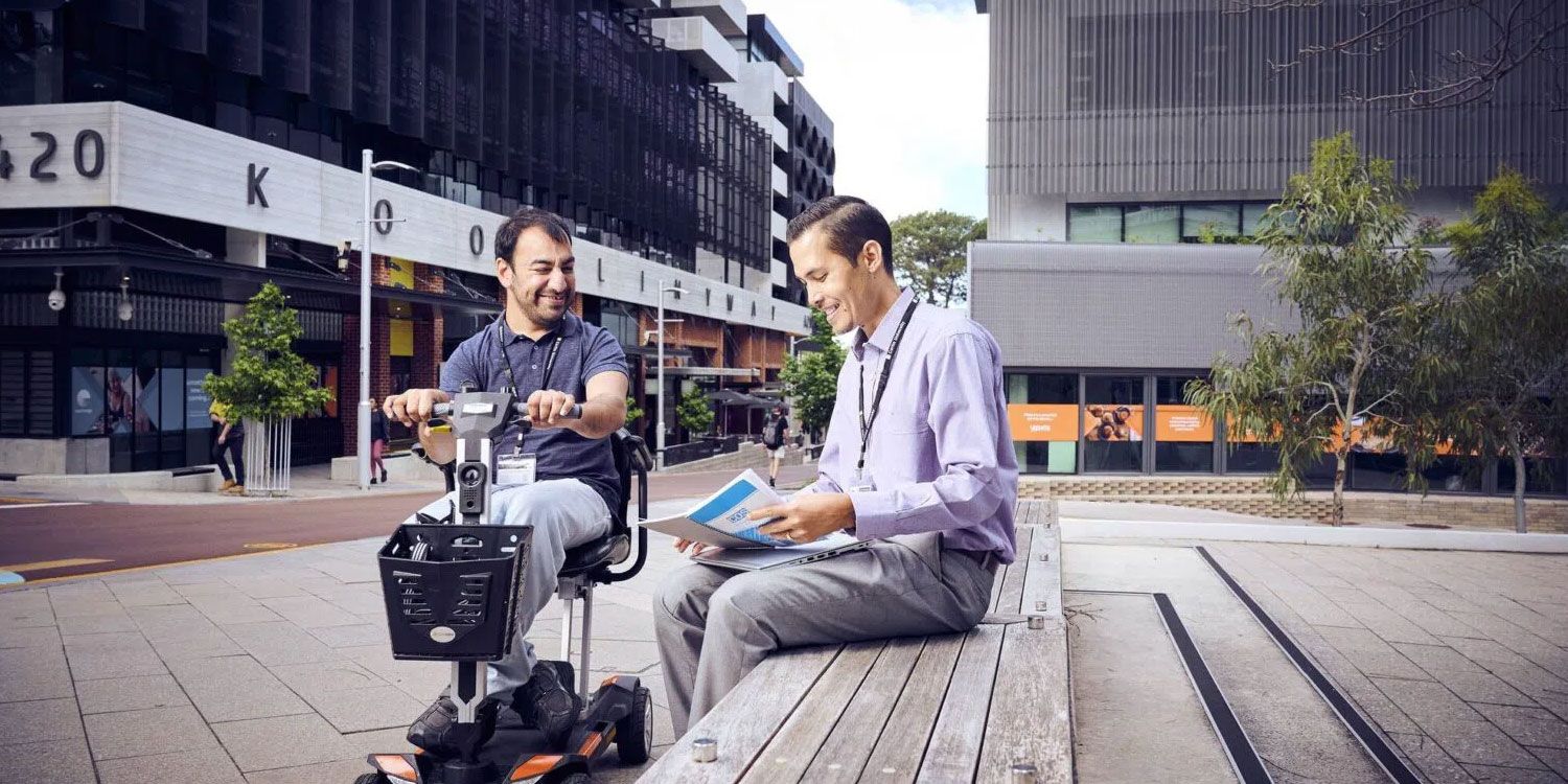 Person sitting helping another person on a motorised chair at Curtin