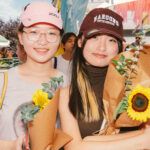 Two students wearing caps and holding sunflowers.