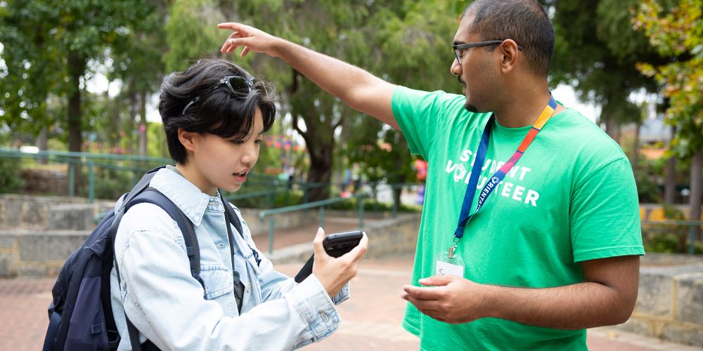 A person pointing at something while another person looks at their phone.