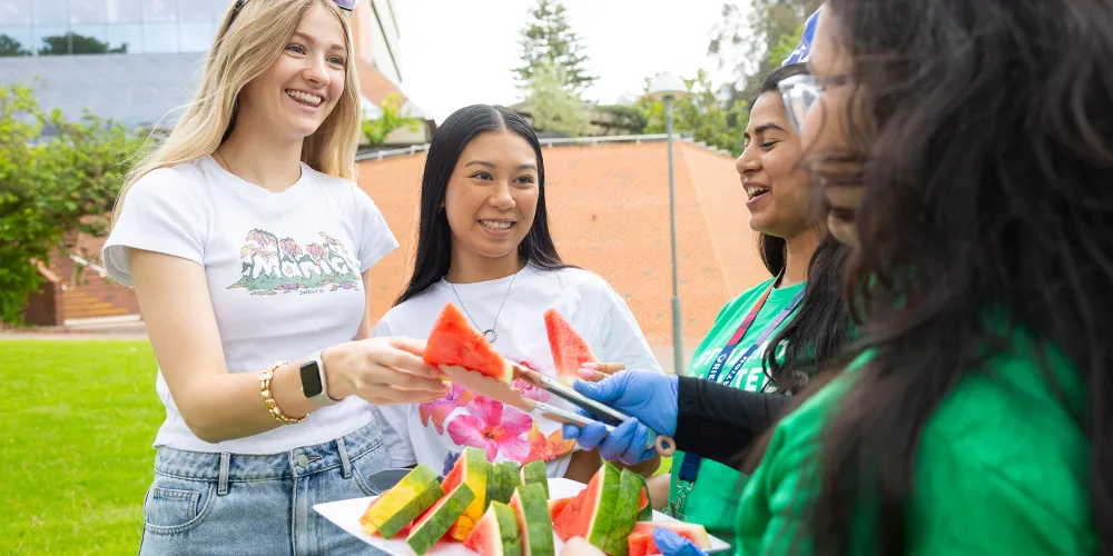 Two students grabbing slices of watermelon from New to Curtin Mentors.