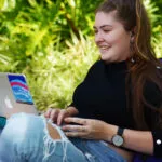 A person sitting on a beanbag and smiling at a laptop.