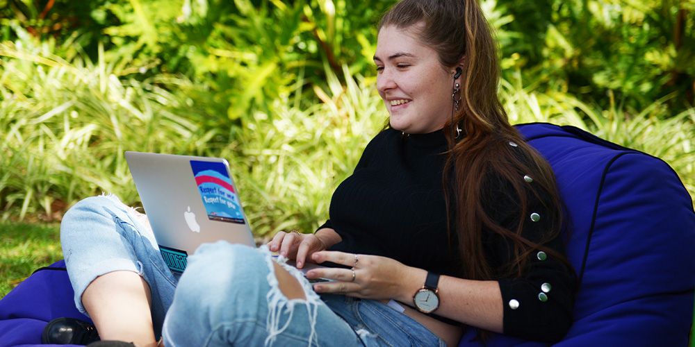 A person sitting on a beanbag and smiling at a laptop.