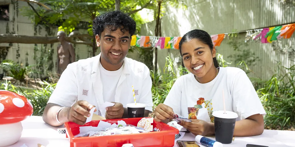 Two people doing crafts at an outdoor table with decorations and greenery.