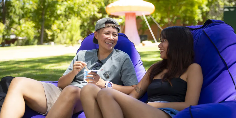 Two people smiling on a blue bean bag in a park.