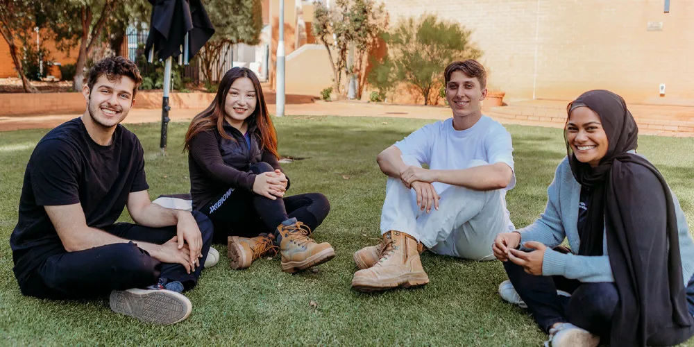 Group of people sitting on grass outdoors, wearing casual clothing and boots.