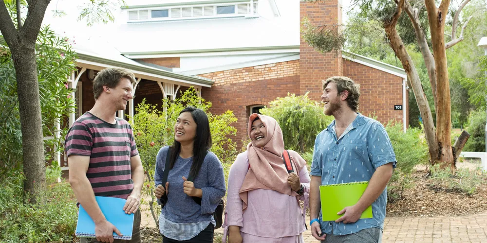 Four people standing outside a brick building, holding folders and backpacks.