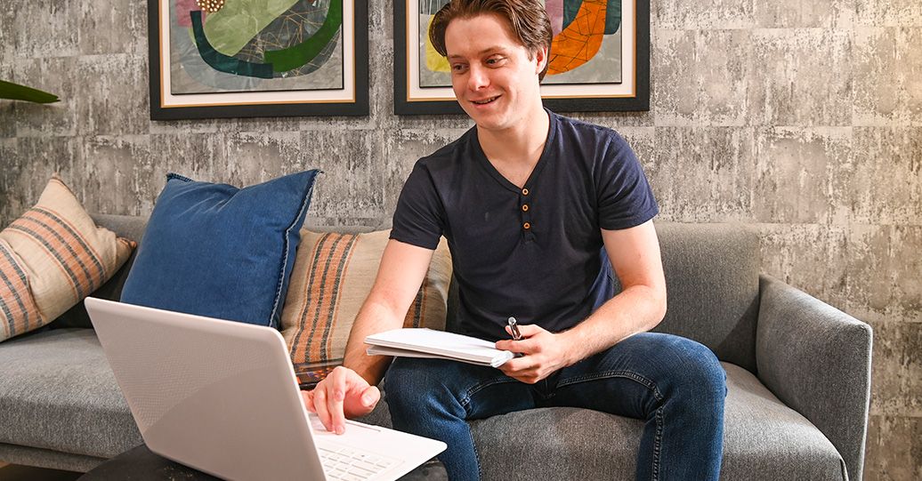 Student using a laptop and notebook while sitting on a couch.
