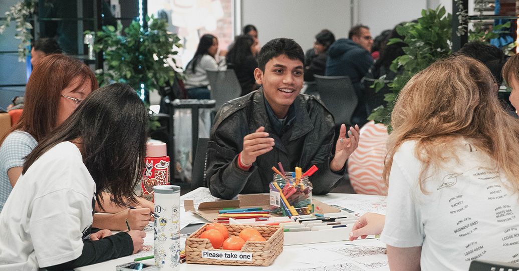 Students collaborating at a table with markers during an indoor campus activity. - play video