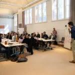 A student speaks in front of a room full of people.