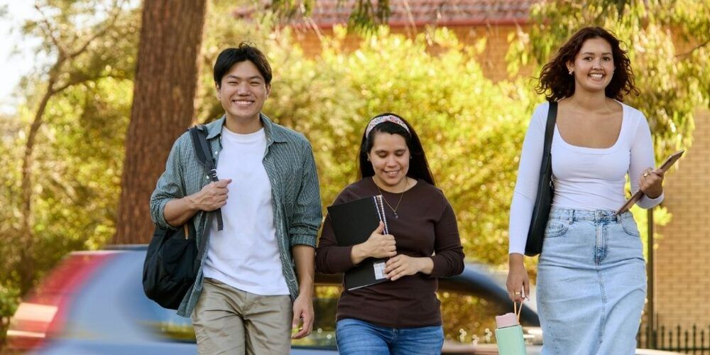 Three students walking to Campus with cars moving in the background
