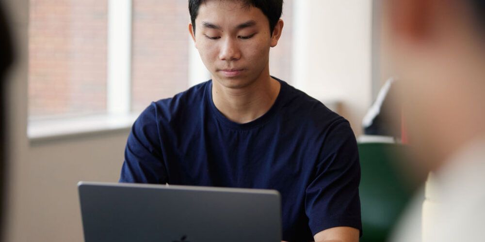 A student looks at their laptop while sat down