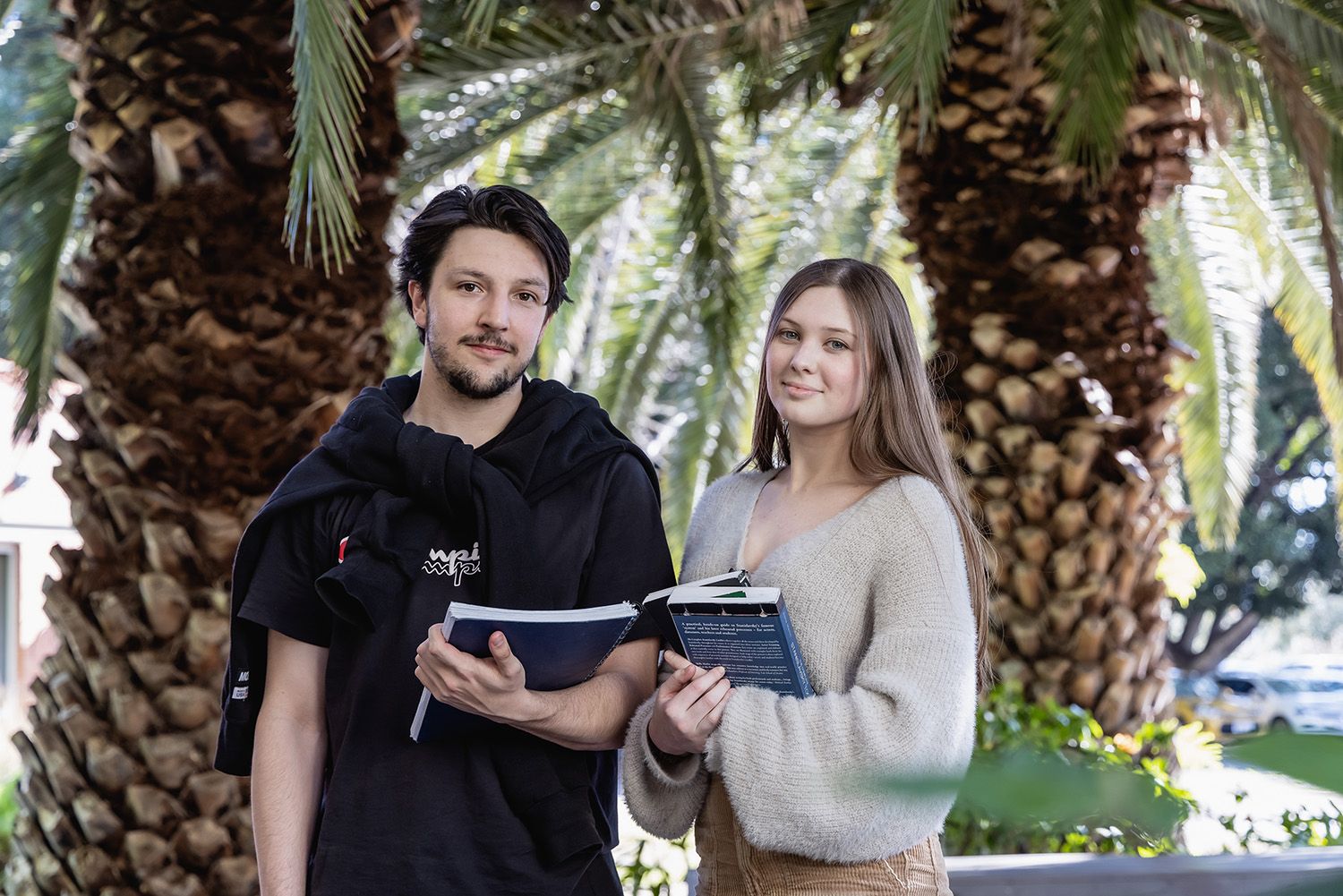 Two students with books with trees in the background