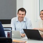 Three business students sitting at a table discussing what's on their laptops