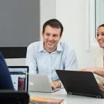 Three business students sitting at a table discussing what's on their laptops