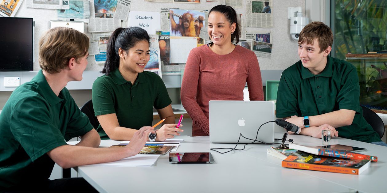 Three high school students sitting at a table talking to a teacher