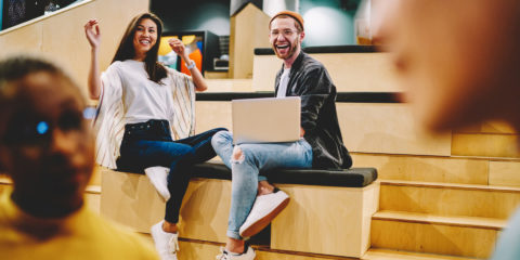 woman and man sat on a bench with laptop laughing