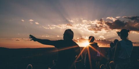 A man pointing to the sky with the sunset in the background