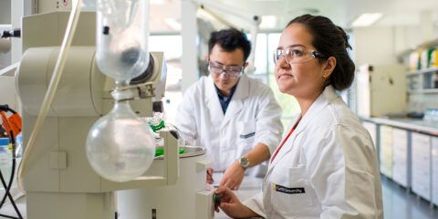 Two students working on science equipment, wearing lab coats