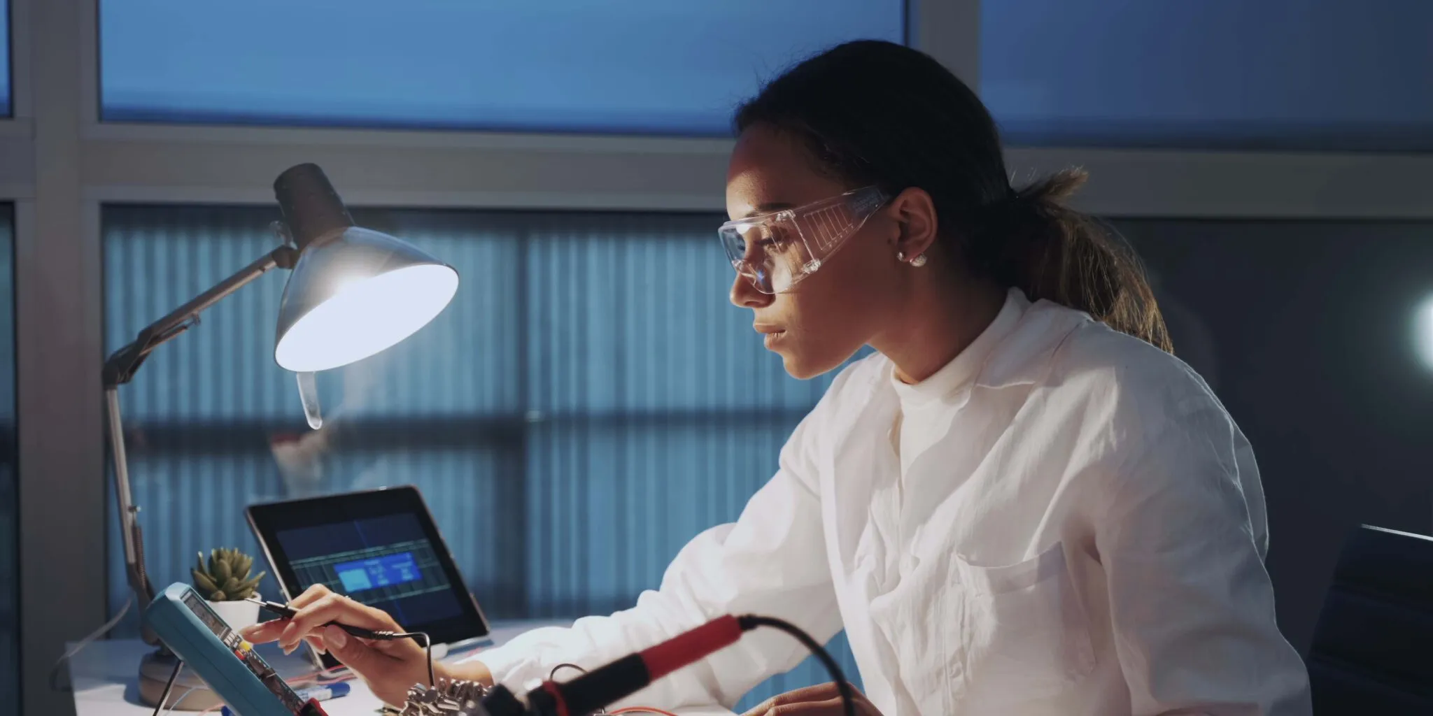 Female scientist using technology at a desk beside a lamp