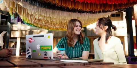 Two students sitting together outside with a laptop