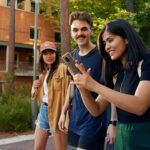 three students walking on campus with a mobile phone