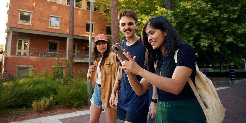 three students walking on campus with a mobile phone