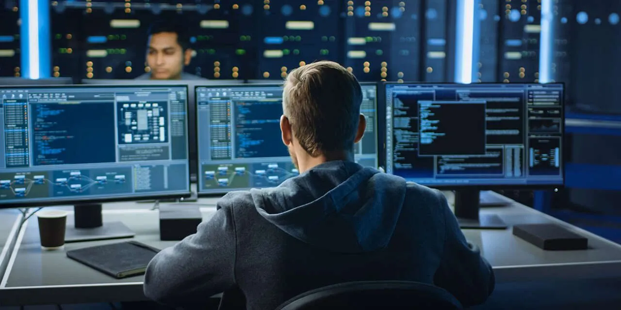 Man facing multiple computer monitors reading code