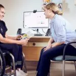 Female student using wheelchair reviewing disability resources with Curtin staff member