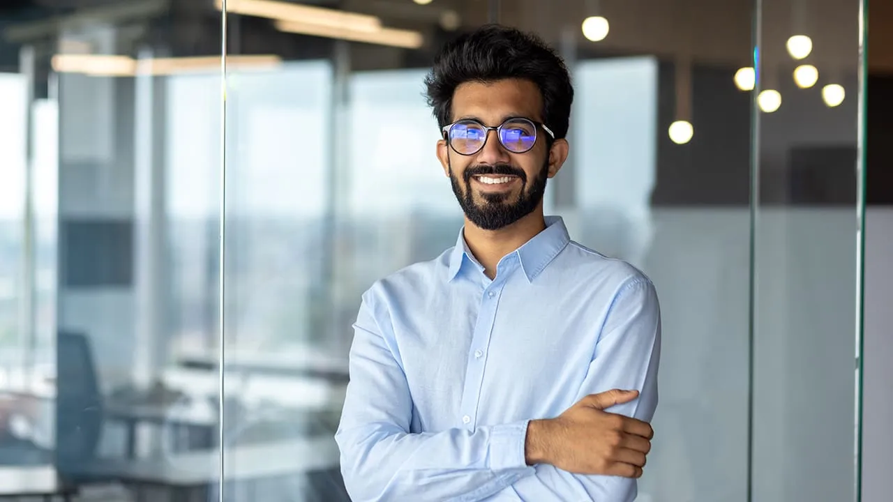 Young male professional with beard and glasses standing in front of glass wall