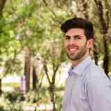 dark haired curtin student rob di giovanni standing against an out of focus background of green and brown trees