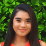 Woman smiling with greenery behind her.