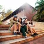A group of students sitting outside on stairs, chatting and enjoying the evening sun.