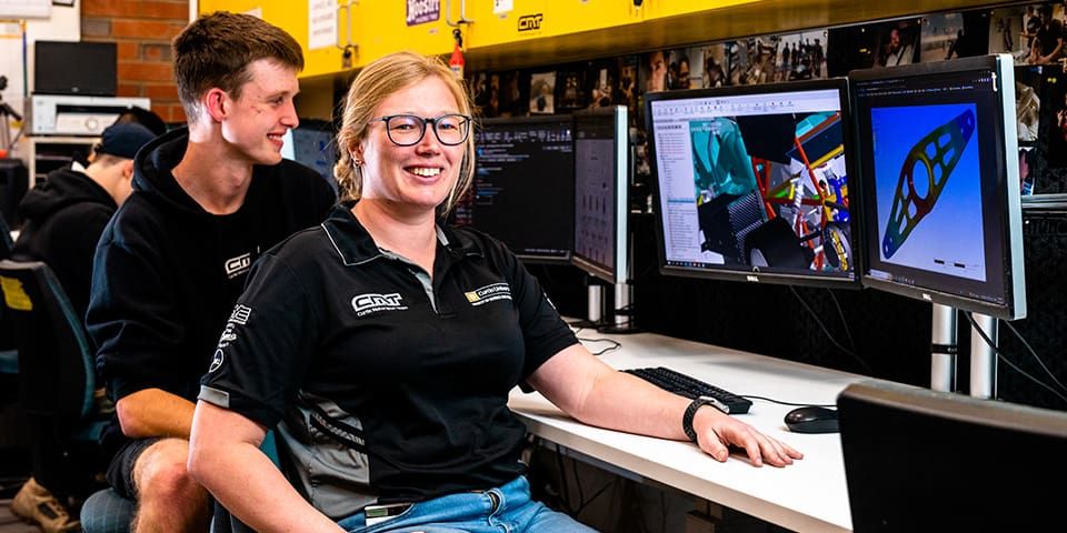 Happy female Mechanical Engineering student with glasses, sitting at a computer desk.