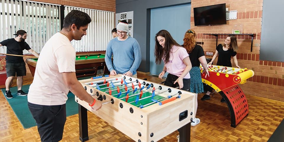 Students playing foosball and pool at the Erica Underwood House