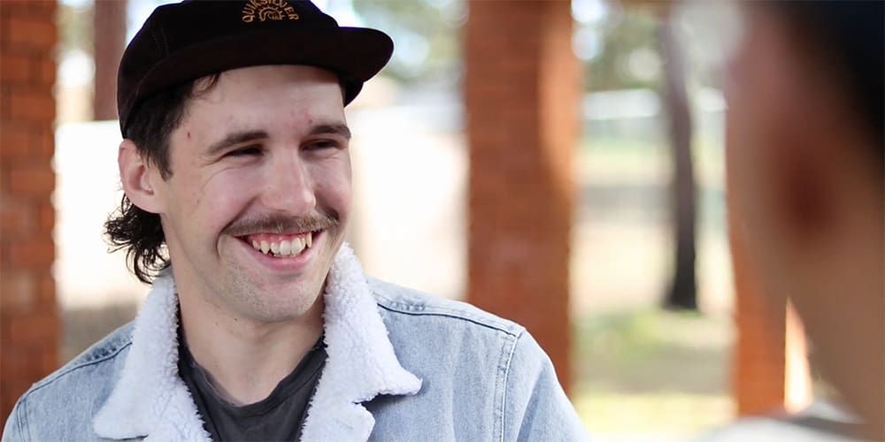 Young, smiling student with a moustache, wearing a black cap - play video
