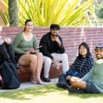 A group of students on Perth campus, sitting on a wooden bench and the grassed area.