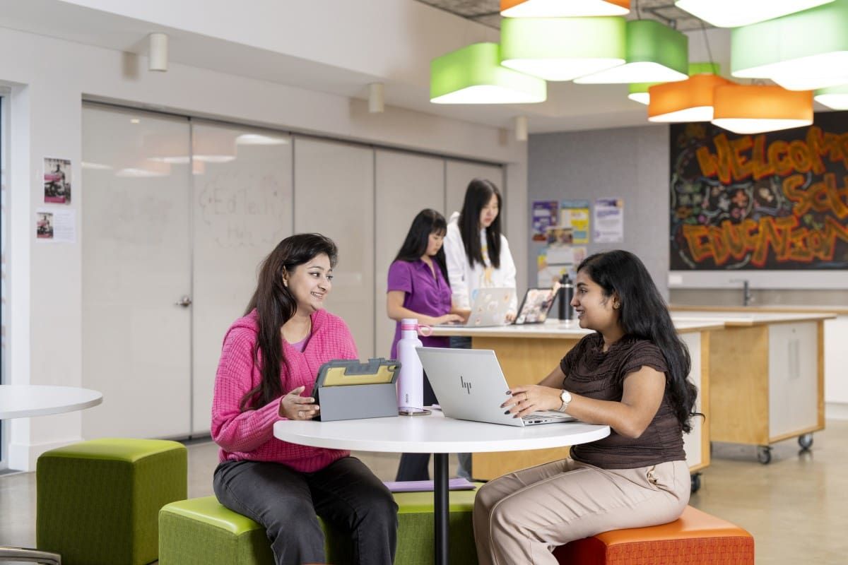 Two Curtin Educational Studies students sitting at a table together, talking.