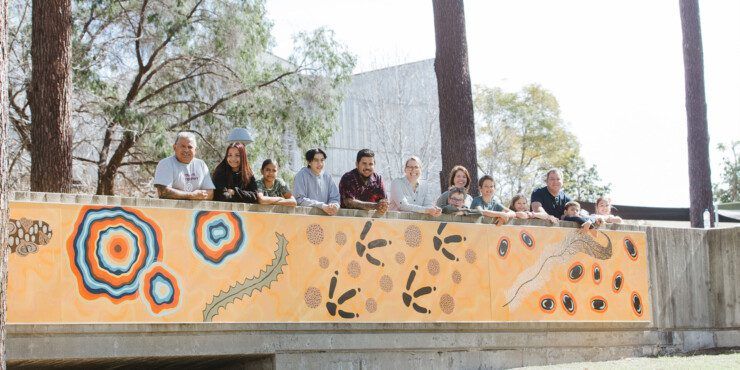 A large group of people standing on a bridge covered in Aboriginal art on the Curtin Perth campus.