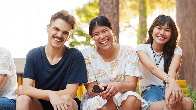 Three happy students sitting in the sun and smilingf