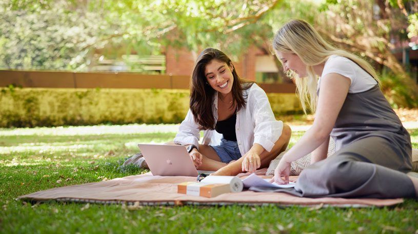 Two students sitting on a picnic blanket and studying